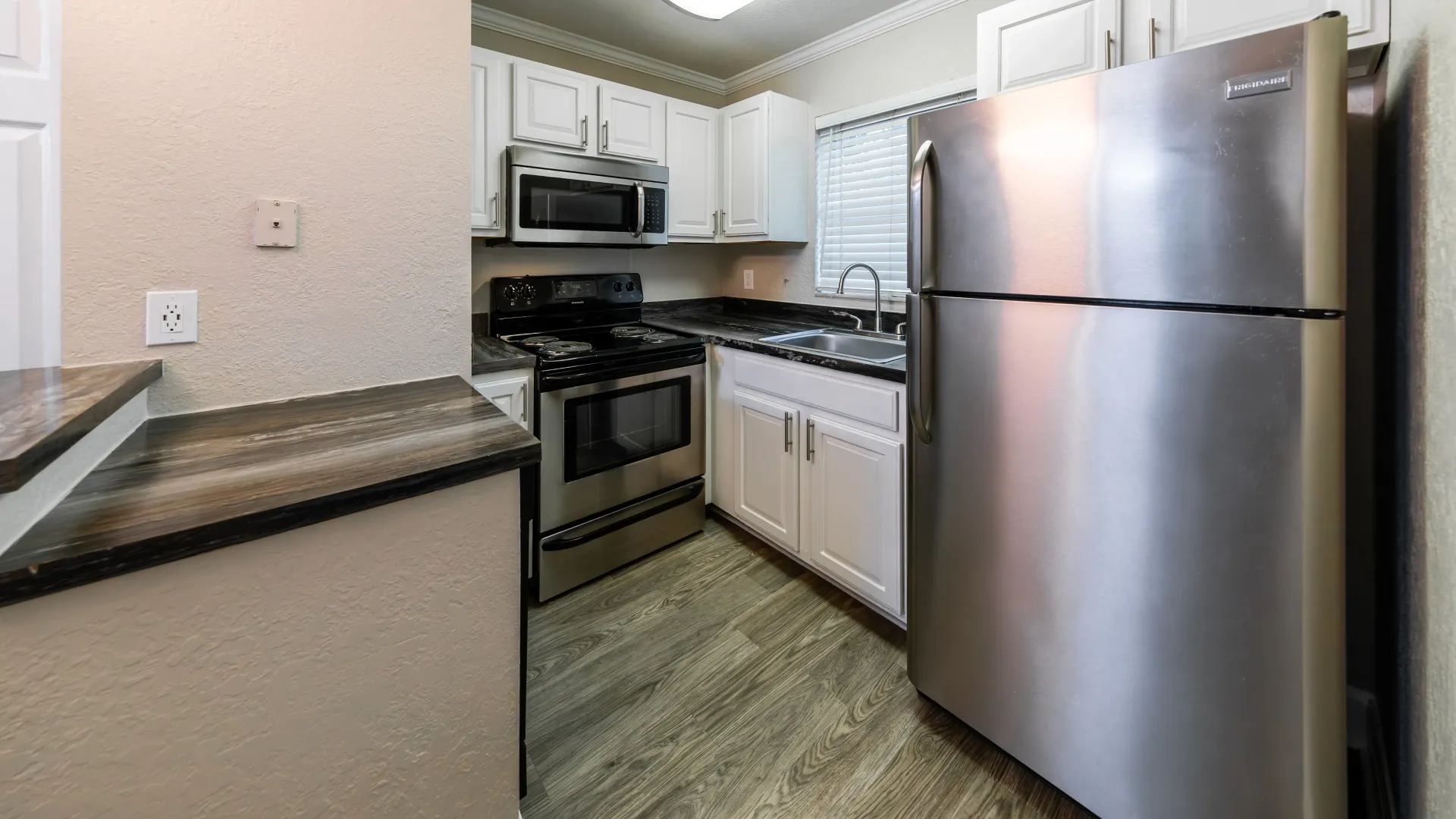 A cozy kitchen featuring stainless-steel appliances, including a gleaming refrigerator, above-stove mounted microwave, and dishwasher, accompanied by black fusion countertops and a convenient USB outlet.