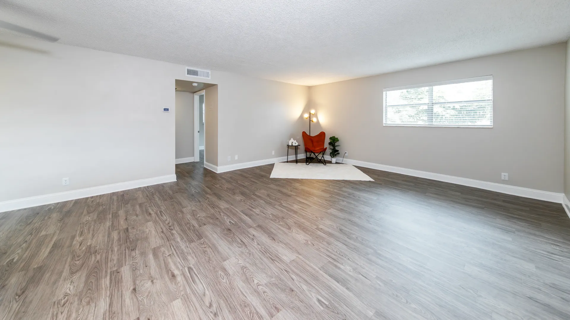 A generously-sized living room with cozy wood-style flooring and a double wide window for sunny, vibrant setting.