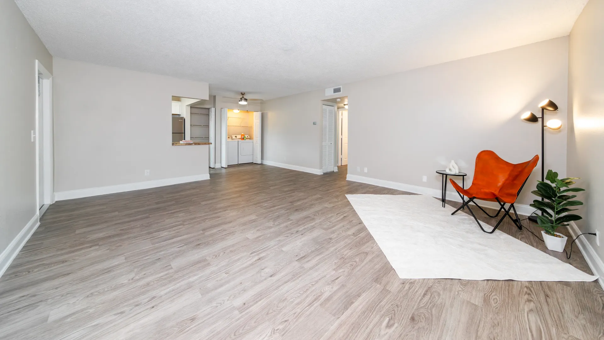 A wide-open living room space showing a clear line of sight into the quaint kitchen, conveniently located laundry appliances, and an added storage pantry—everything you need to live comfortably.