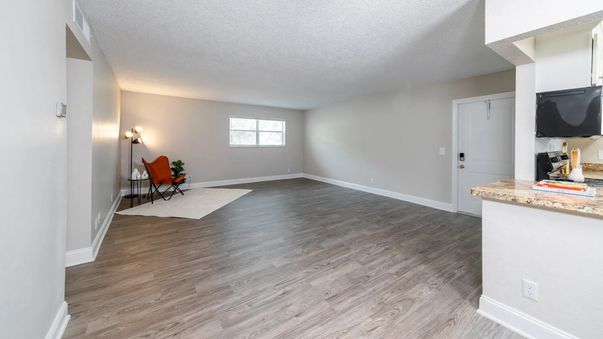 A generously spaced living room adorned with wood-planked floors and a double window that welcomes abundant sunlight, creating an inviting and refreshing atmosphere for relaxation.