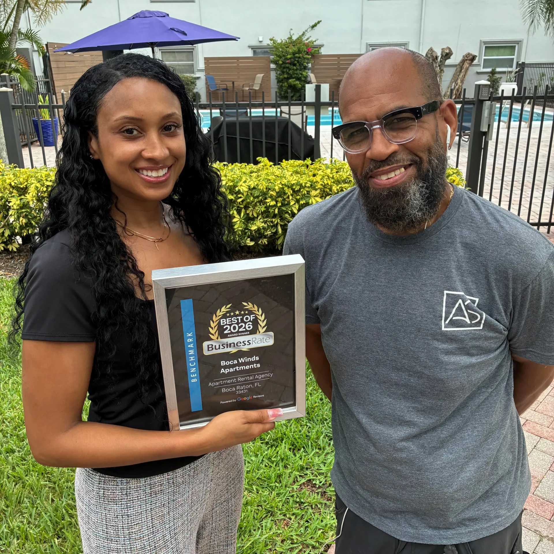 Boca Winds Apartments staff members holding the BusinessRate Best of 2026 Award plaque in front of the community's pool and landscaped grounds.