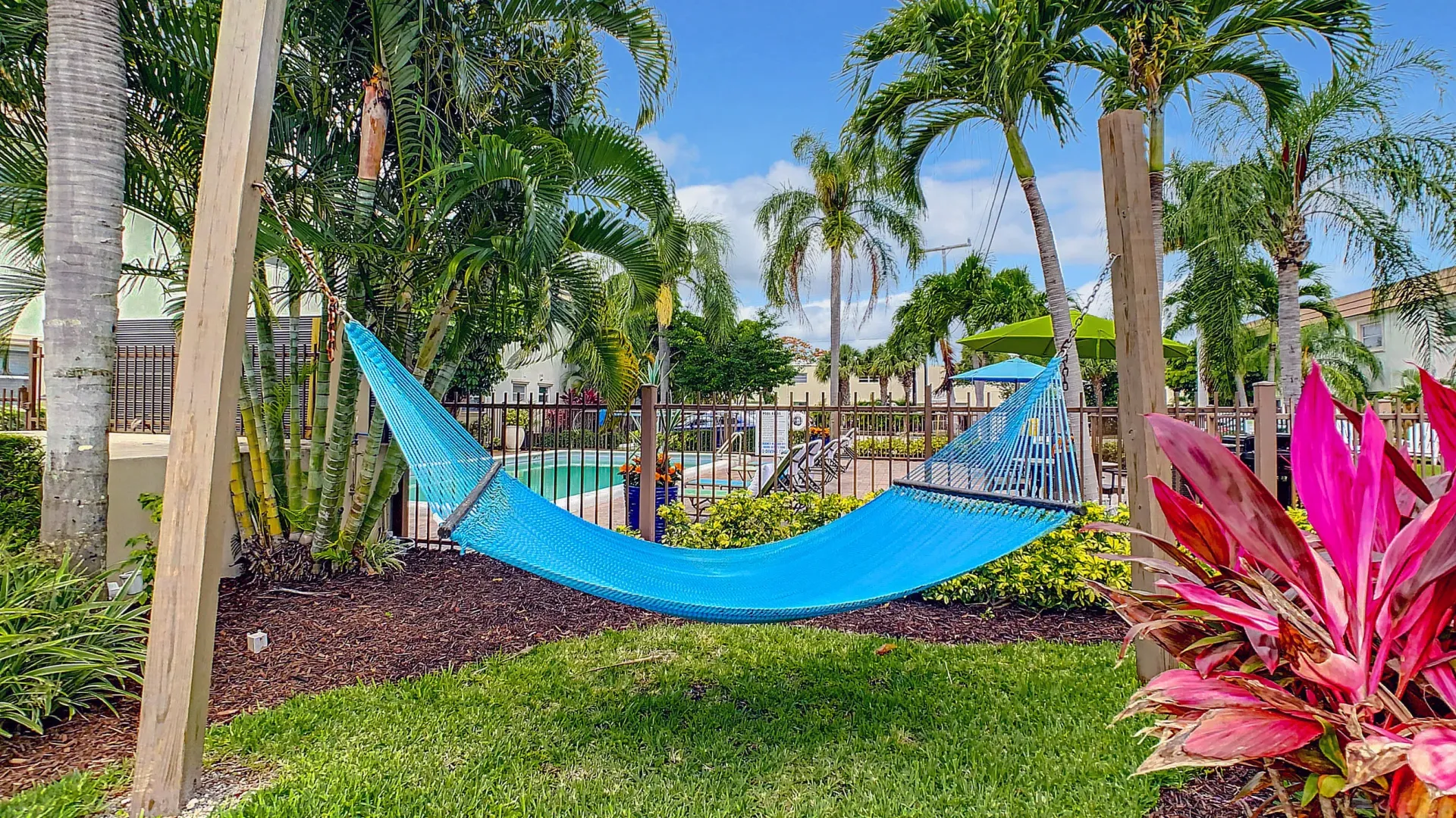 A hammock garden beneath palm trees just outside the gated pool area inviting residents to relax and rejuvenate in the serene abode. 