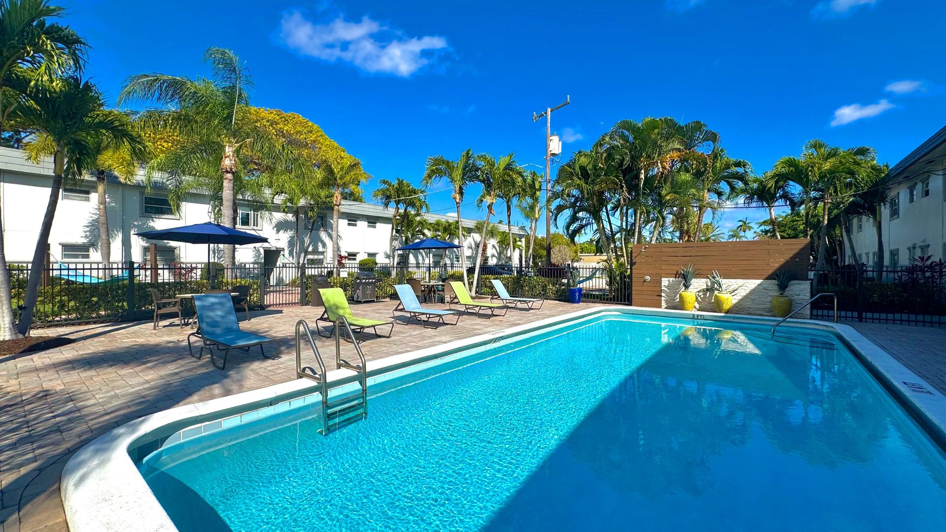 Outdoor swimming pool surrounded by palm trees and seating at Boca Winds Apartments.