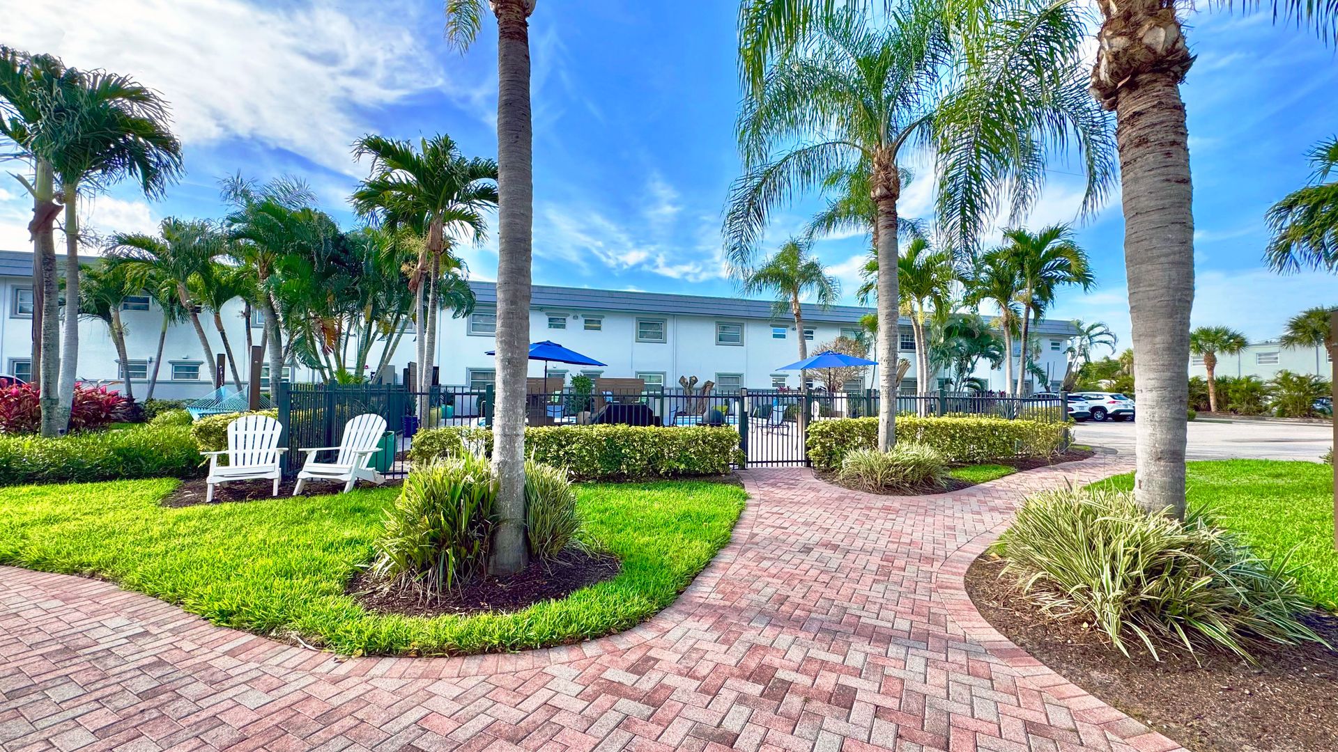 Tropical landscape featuring a winding walkway, Adirondack chairs, and a relaxing pool area.