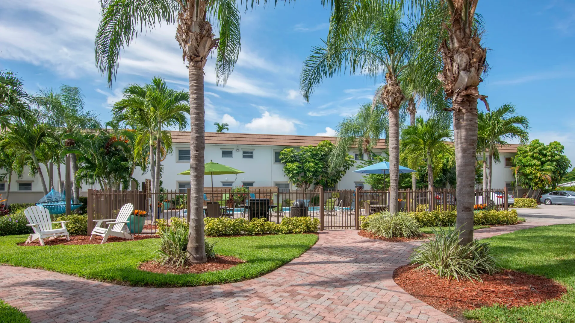A paved walkway winding through lush, tropical landscaping, leading to the vibrant gated pool area.