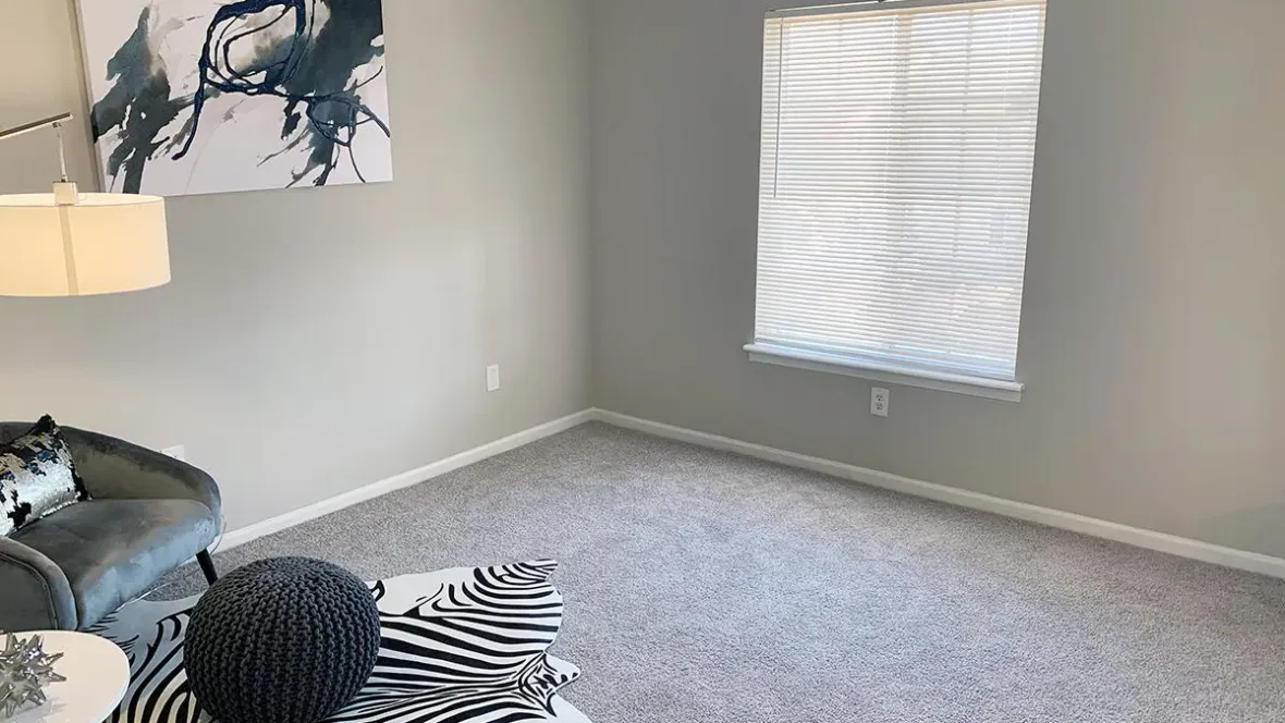 A bedroom with a window with privacy blinds and plush, grey carpet