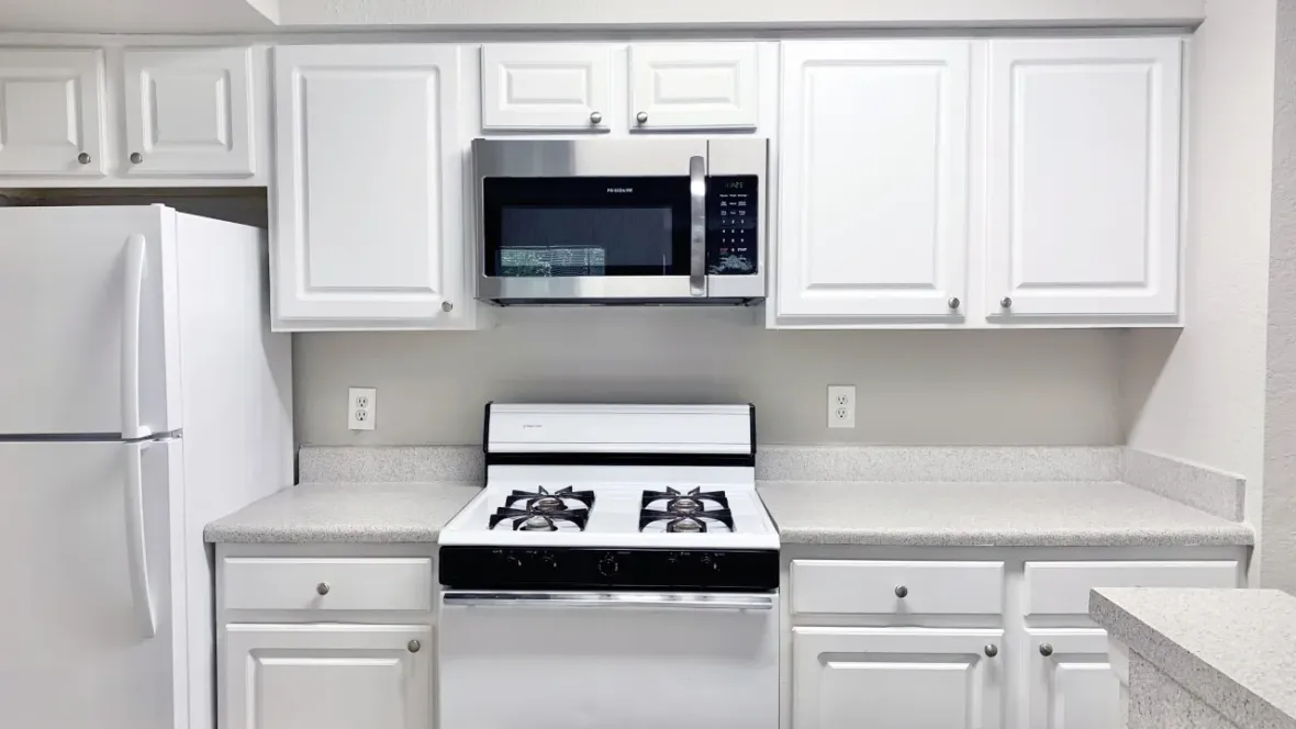 An angle of the kitchen that shows crisp, white cabinetry along with a refrigerator, stove, and built-in microwave.