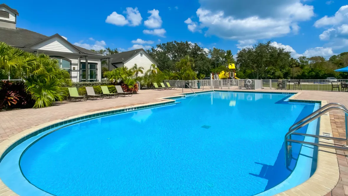 A pool of bright blue water surrounded by an expansive sundeck of pavers and ample lounge chairs.