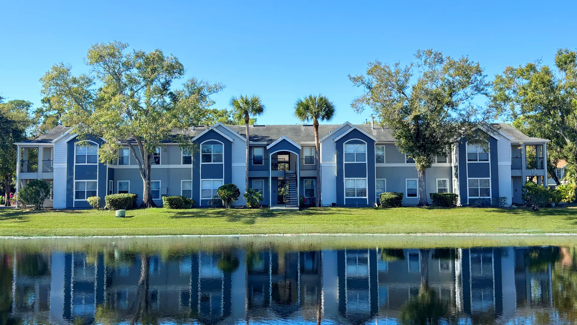 Exterior view of Eden Pointe Apartments in Bradenton, Florida with lake reflection and palm trees.