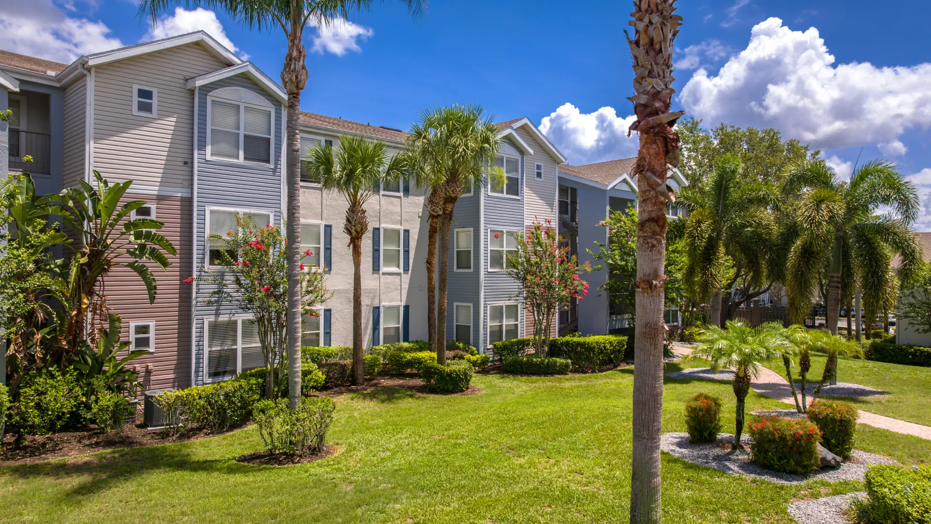 Exterior view of Ashton Chase Apartments with palm trees, tropical plants, and a manicured lawn.