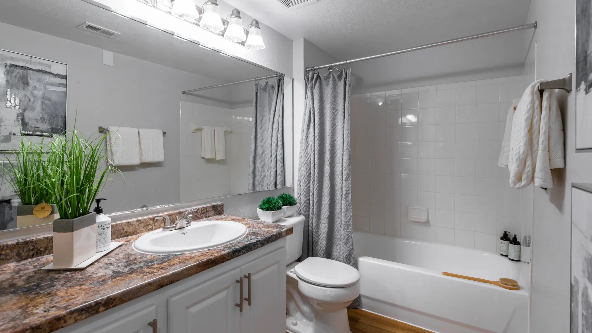 Modern bathroom at Ashton Chase featuring granite-style counters, white tile shower and tub combo, and modern brushed-nickel fixtures.
