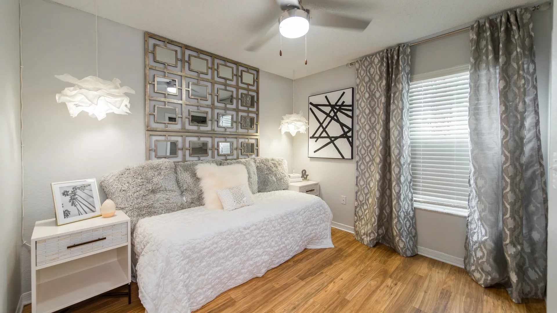 Guest bedroom with decorative mirror wall, modern lighting, and cozy bedding at Ashton Chase Apartments.