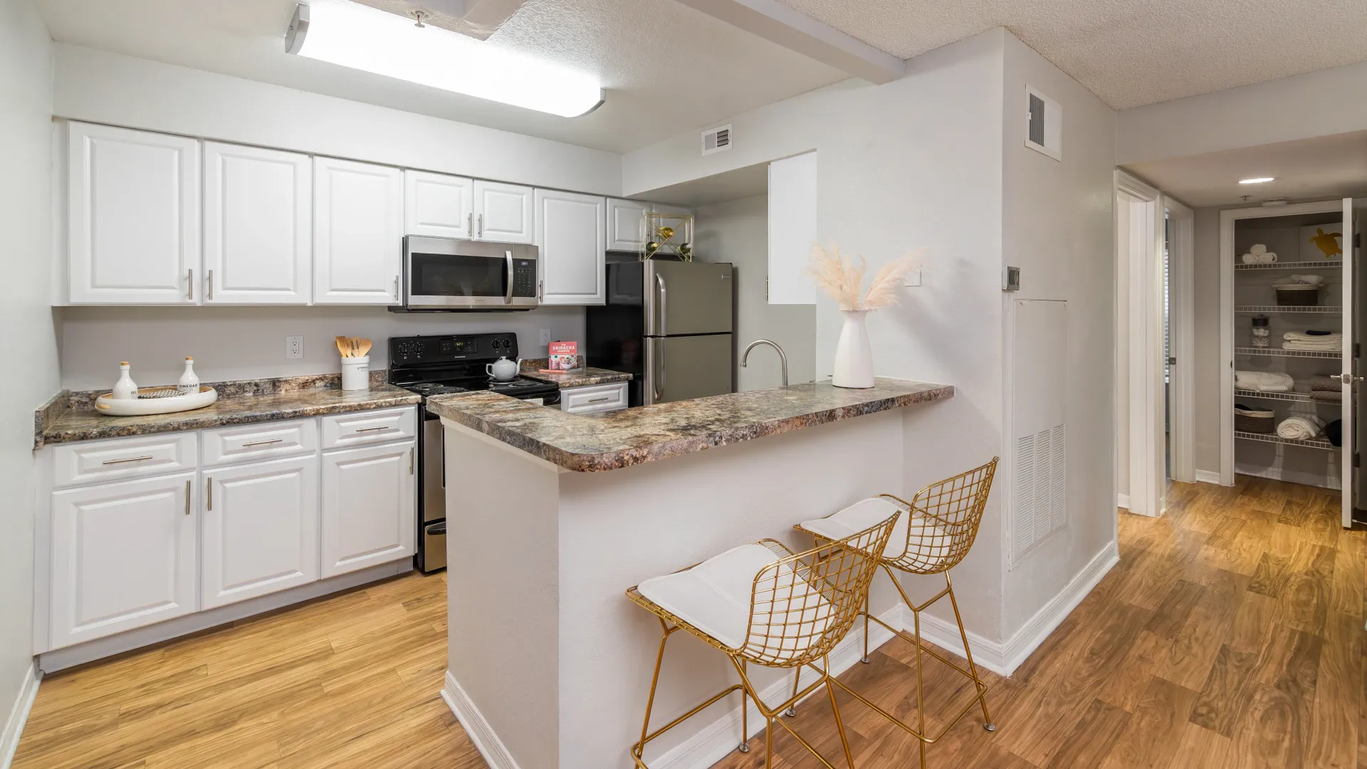 Modern kitchen with white cabinetry, granite-style counters, and a breakfast bar with gold wire stools at Ashton Chase Apartments.