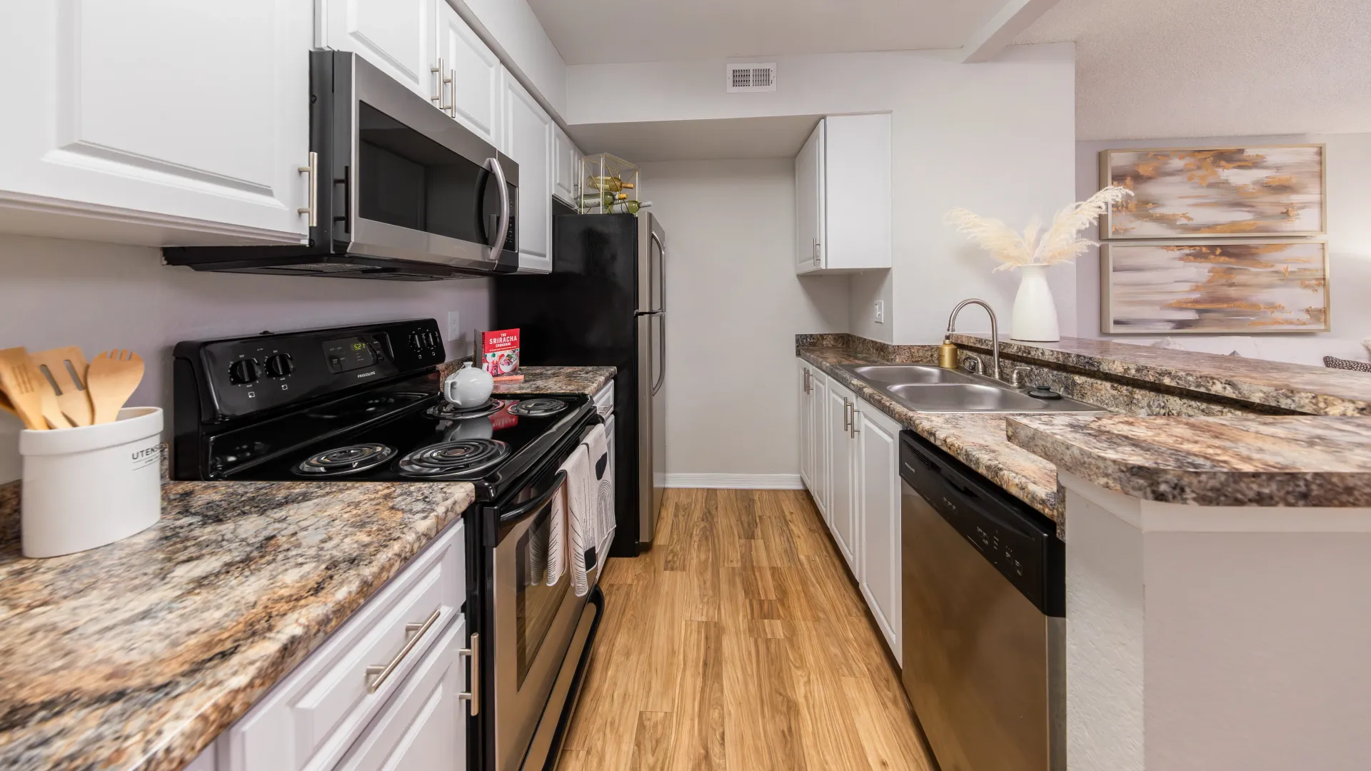 Ashton Chase galley kitchen with stainless steel appliances, granite-style countertops, and white cabinetry.