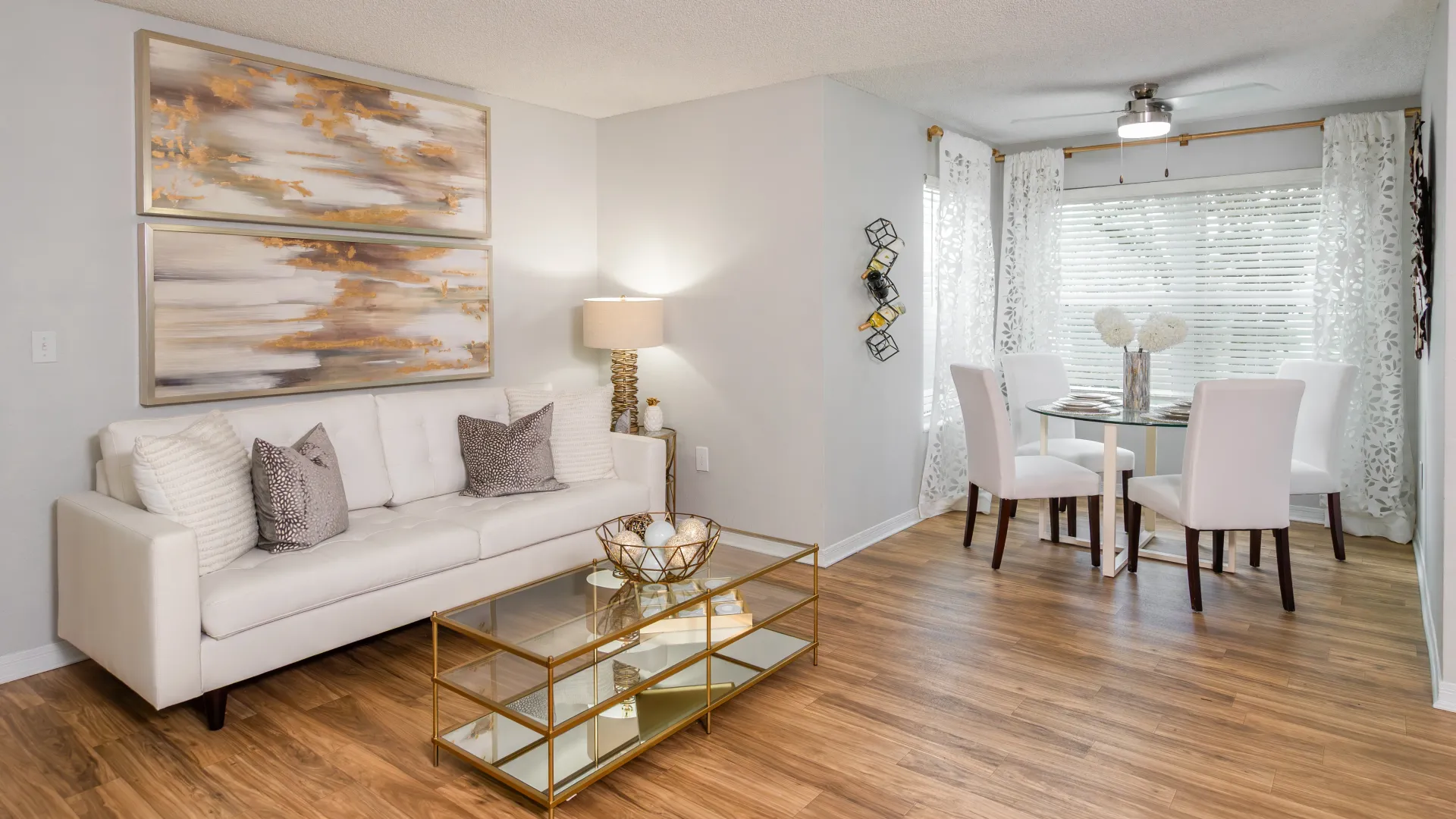 Ashton Chase apartment living room with white sofa and glass coffee table leading into a dining nook with white chairs and round table.