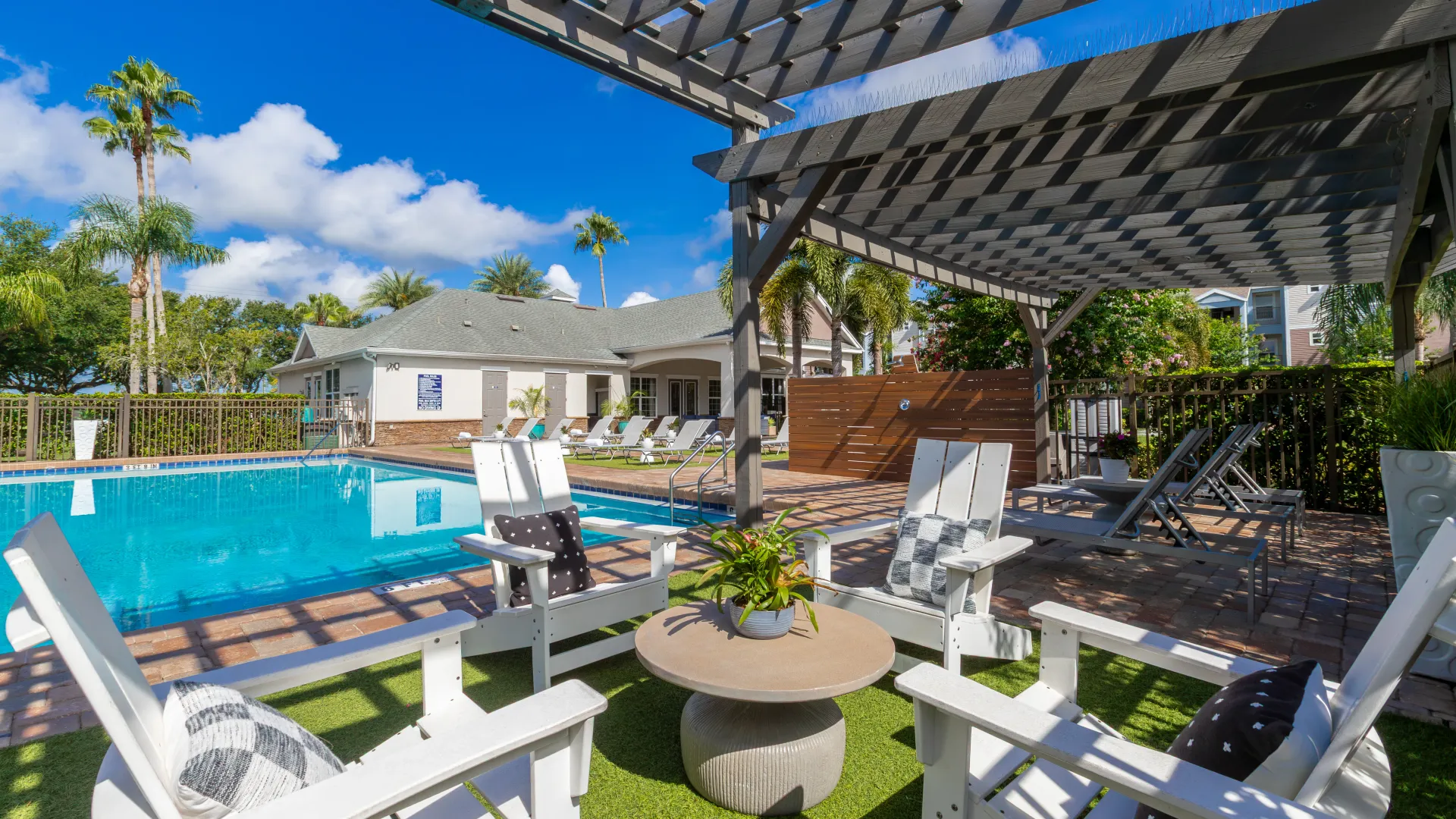 Shaded seating area with Adirondack chairs and a round table beside the pool at Ashton Chase Apartments.