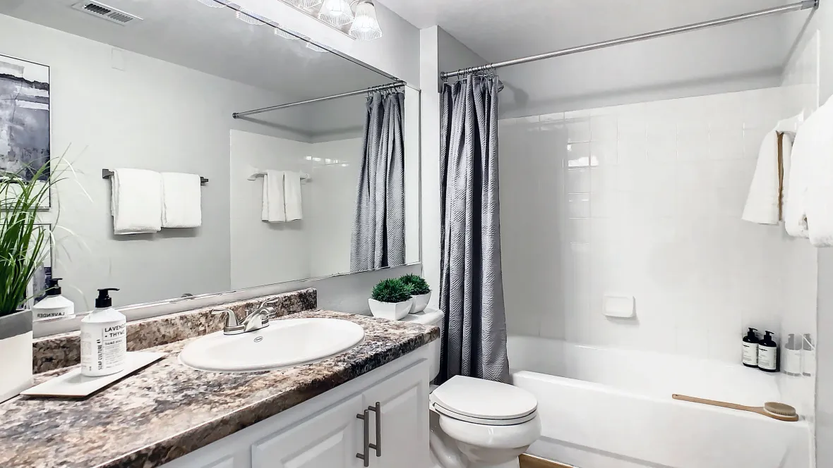 Stylish guest bathroom featuring a crisp white tile shower/tub combo, expansive mirror, and ample countertop space.