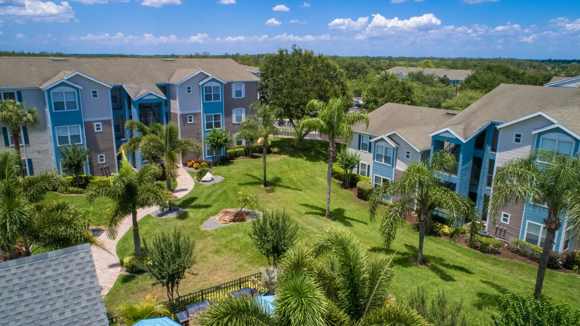Aerial view of the well-manicured tropical landscaping and well-maintained buildings at Ashton Chase Apartments with the Clermont hills over the horizon.