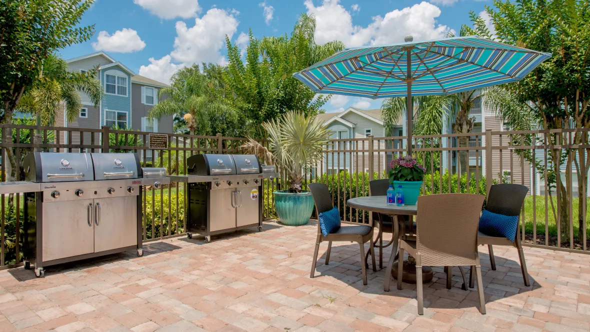 Outdoor kitchen with gas grills and an umbrella covered table and chairs by the pool, perfect for sunny days and social gatherings.