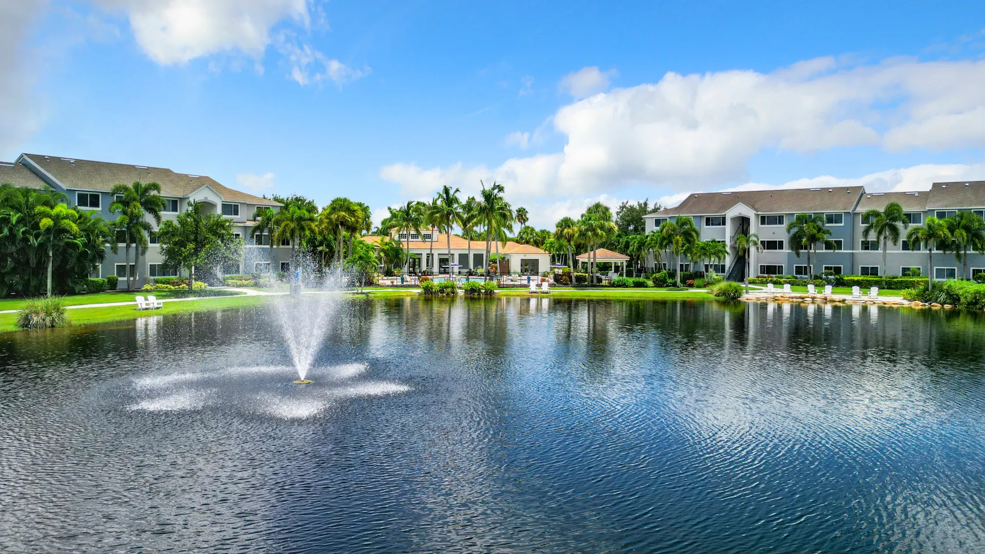 A beautiful lake with a fountain in the foreground, surrounded by apartment buildings and palm trees.