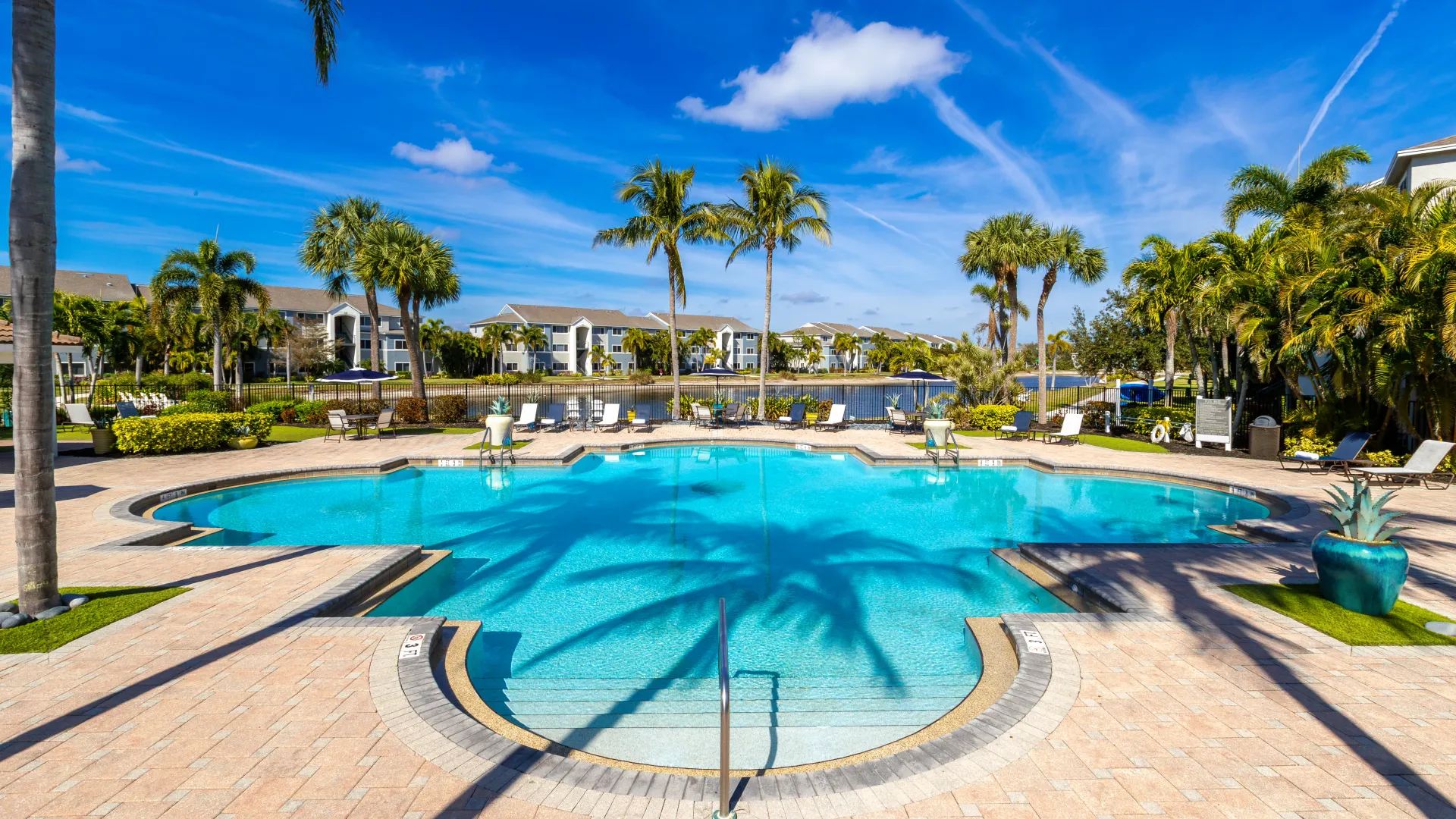 Luxury pool area with palm tree shadows cast on the water, featuring elegant potted plants and a peaceful lakeside setting.