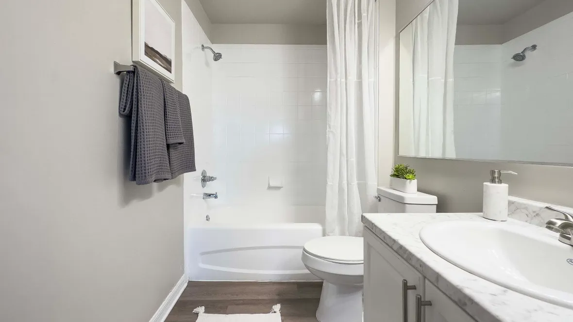 A bright bathroom featuring a shower/tub combo with a pristine white surround, large vanity, and an extensive mirror.