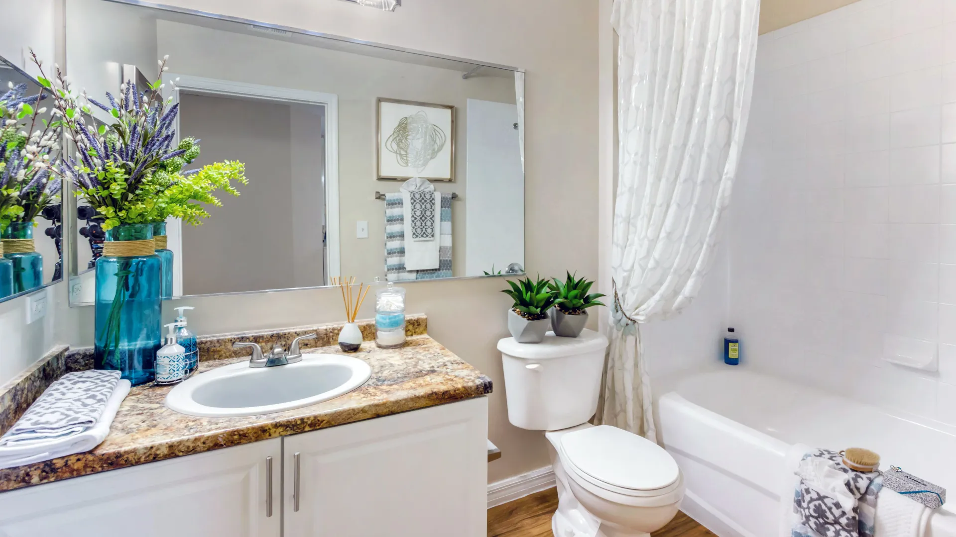 Bathroom at Lexington Palms with golden Mascarella counters, a large mirror, and a bright shower-tub combo.