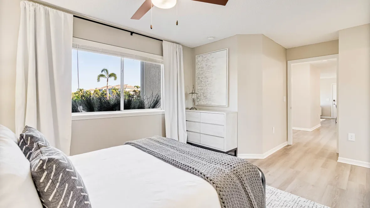 A roomy, versatile guest bedroom where sunlight cascades through the wide window and a bonus ceiling fans draws in additional lighting and comfort. 