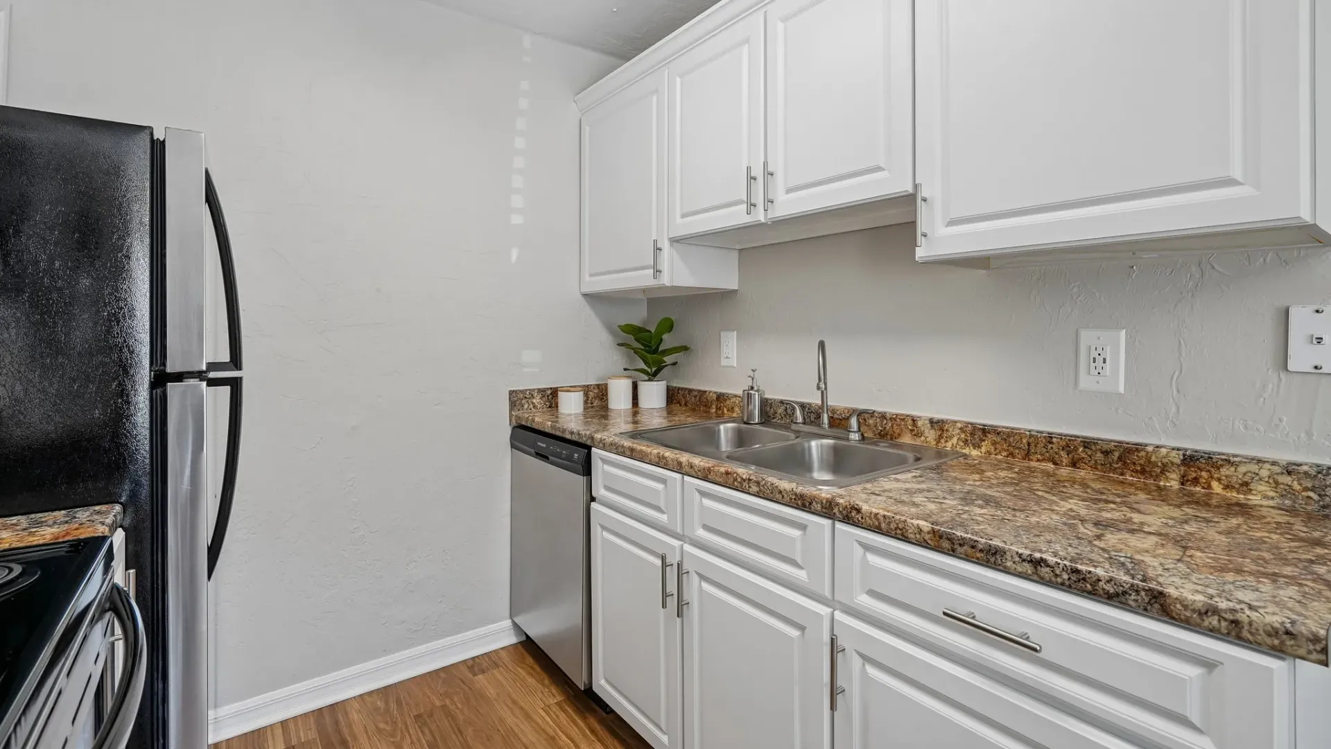 Kitchen interior at Ridgemar Commons featuring white cabinets, granite-inspired countertops, stainless-steel appliances, and wood-style flooring.