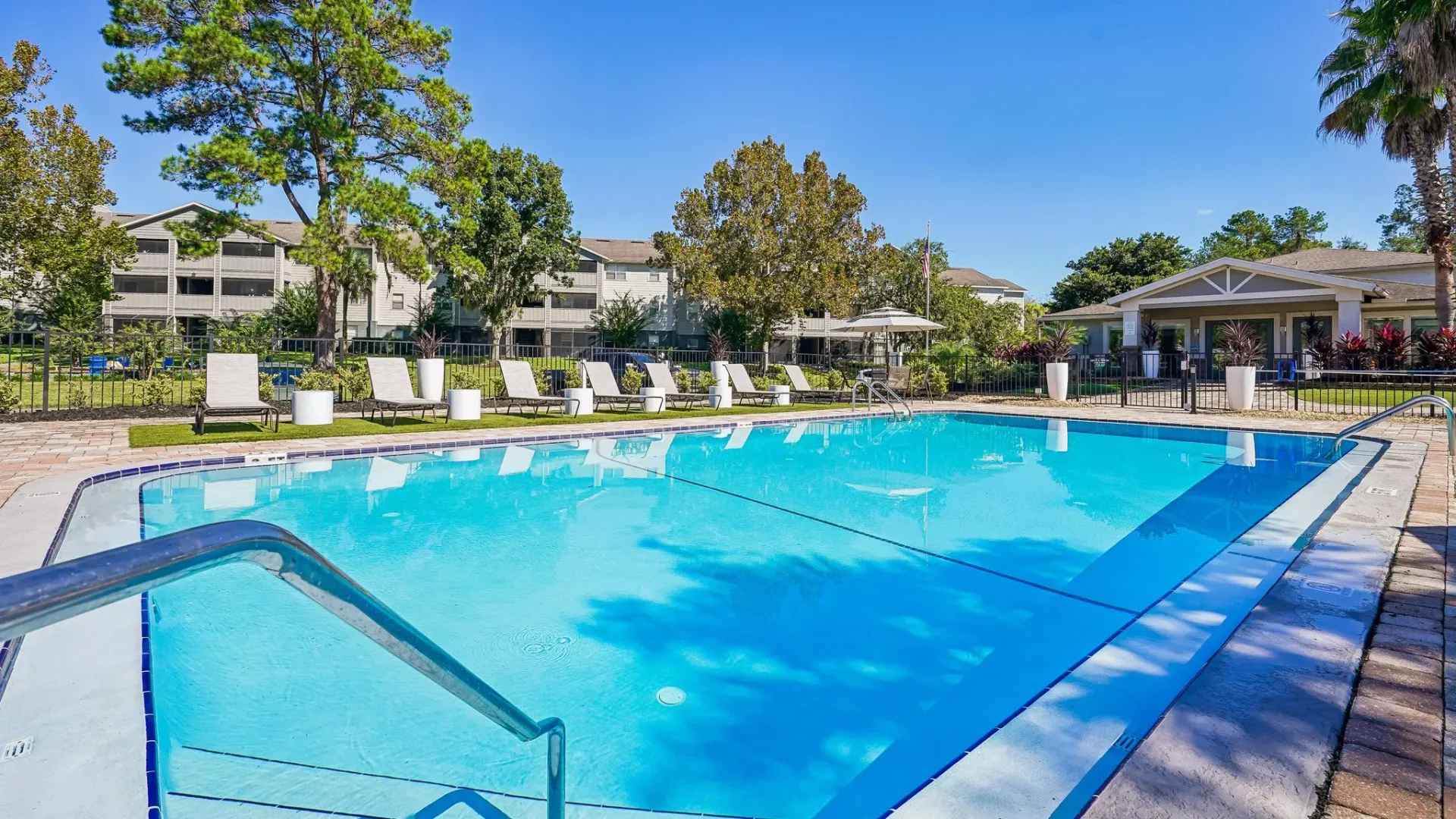 Swimming pool at Ridgemar Commons featuring a large pool, poolside loungers, landscaped grounds, mature trees, and a resort-style sundeck.