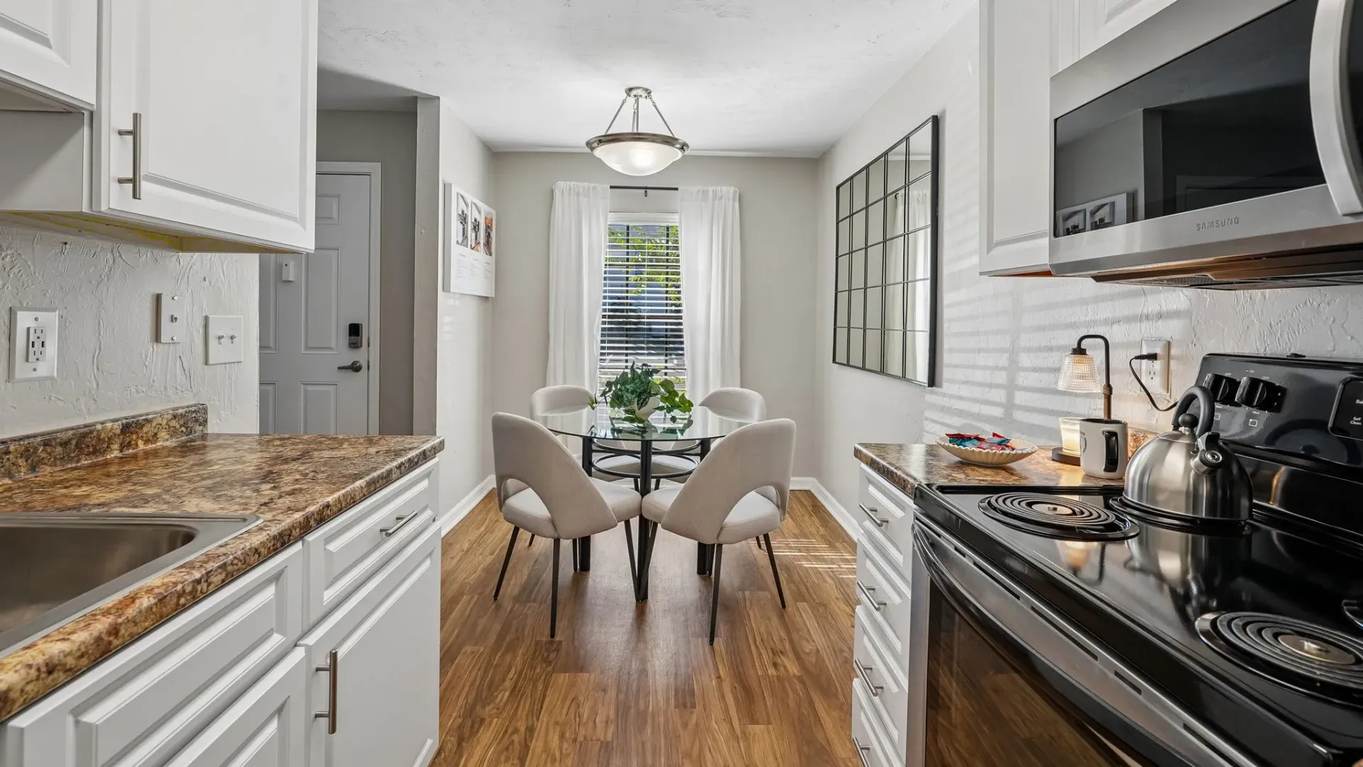 Kitchen and dining area featuring white shaker-style cabinetry, granite-inspired countertops, stainless-steel appliances, wood-style flooring, and a dedicated dining space.