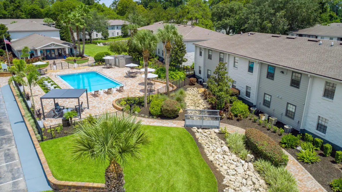  A stunning aerial view showcasing the lush green areas surrounding the resort-style pool, expansive sundeck, and paved walkway.