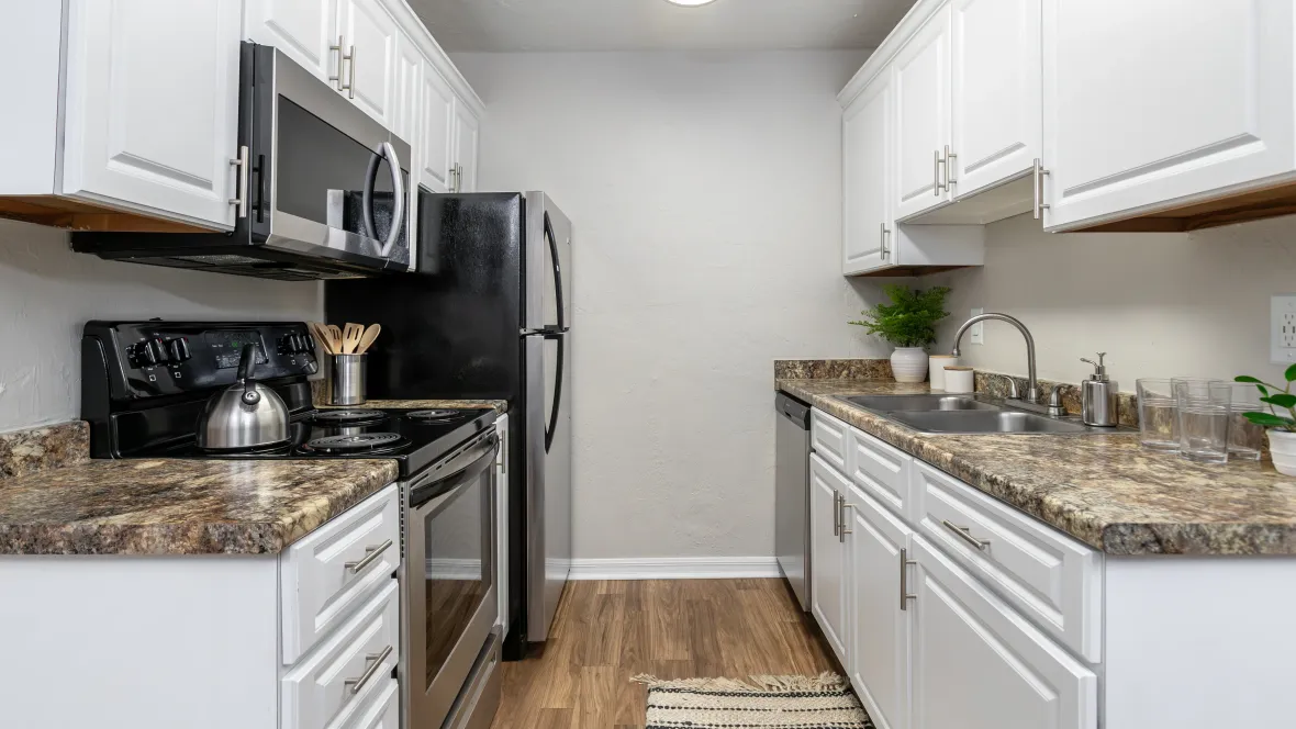 A kitchen showcasing timeless white shaker cabinets, a double sink, stainless-steel appliances, and roomy countertops with complimentary warm brown flooring.