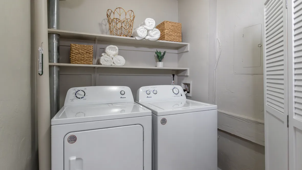 A well-lit laundry room with side-by-side full-size washer and dryer appliances, complemented by two rows of wooden overhead shelving for added storage.