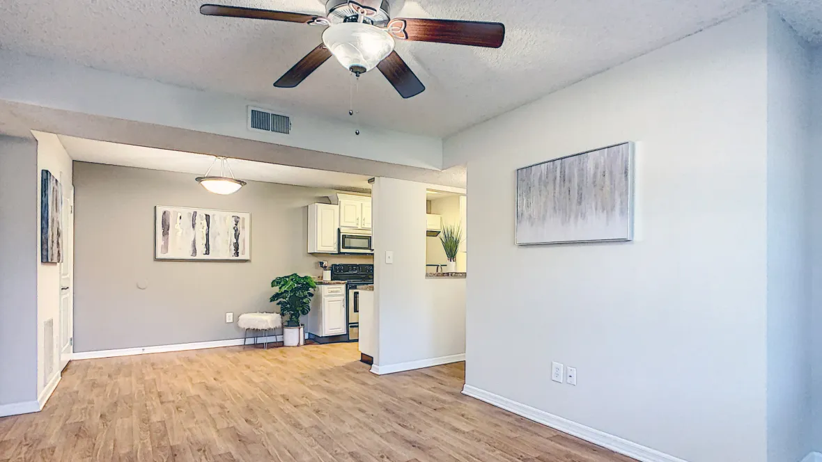 An airy open-concept living space with wood-style flooring, traditional ceiling fan, and a seamless flow from living to dining and kitchen areas.