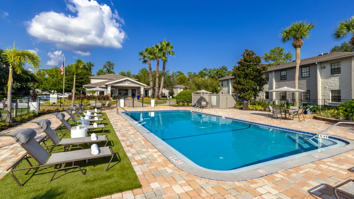 A sprawling paved pool deck around the glistening swimming pool, adorned with loungers on an astroturf carpet, providing a perfect spot for luxe relaxation right at home.