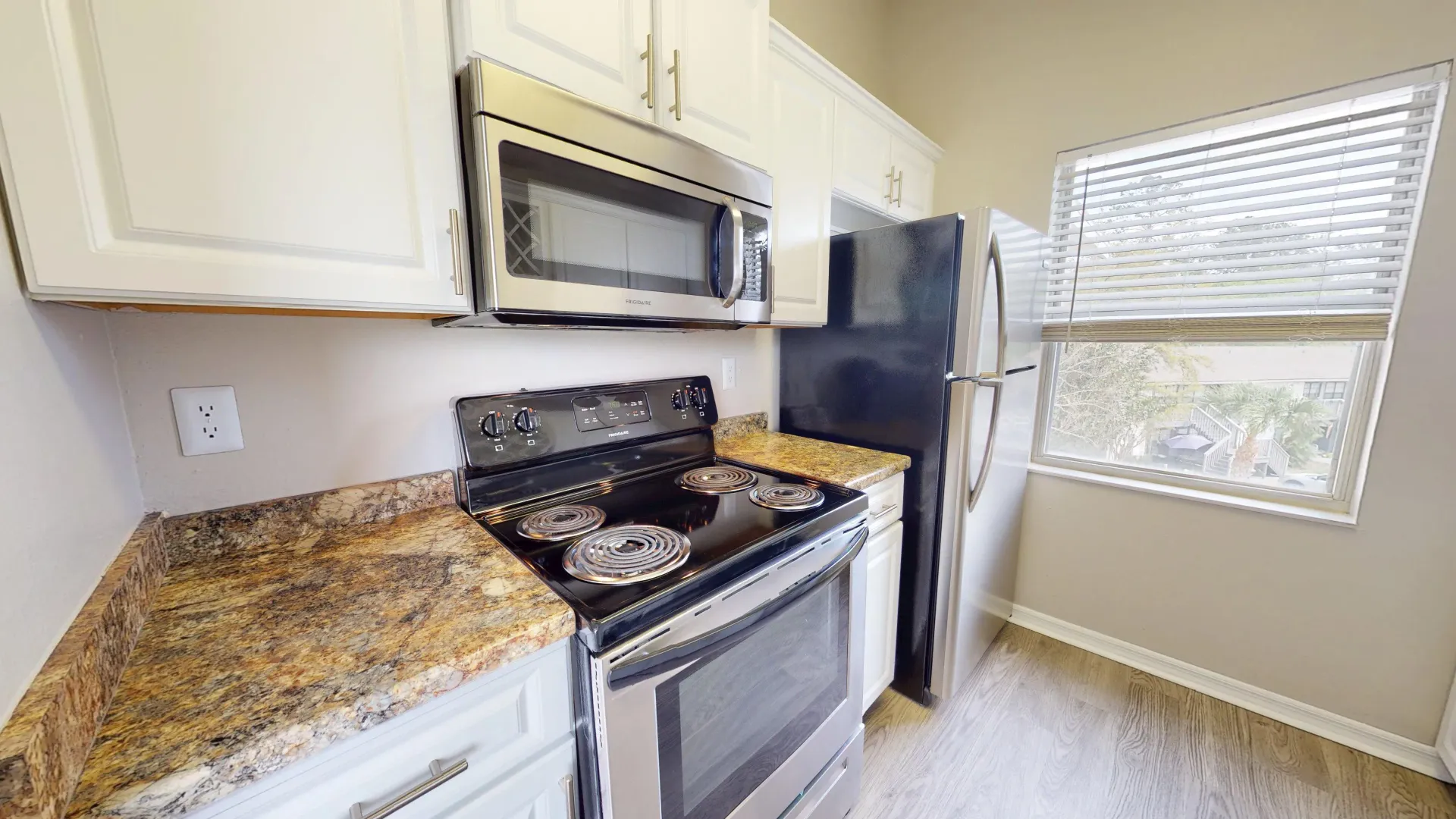 Stainless steel appliances in The City floor plan at Ridgemar Commons featuring a refrigerator, microwave, electric range, white cabinetry, and granite-inspired countertops.