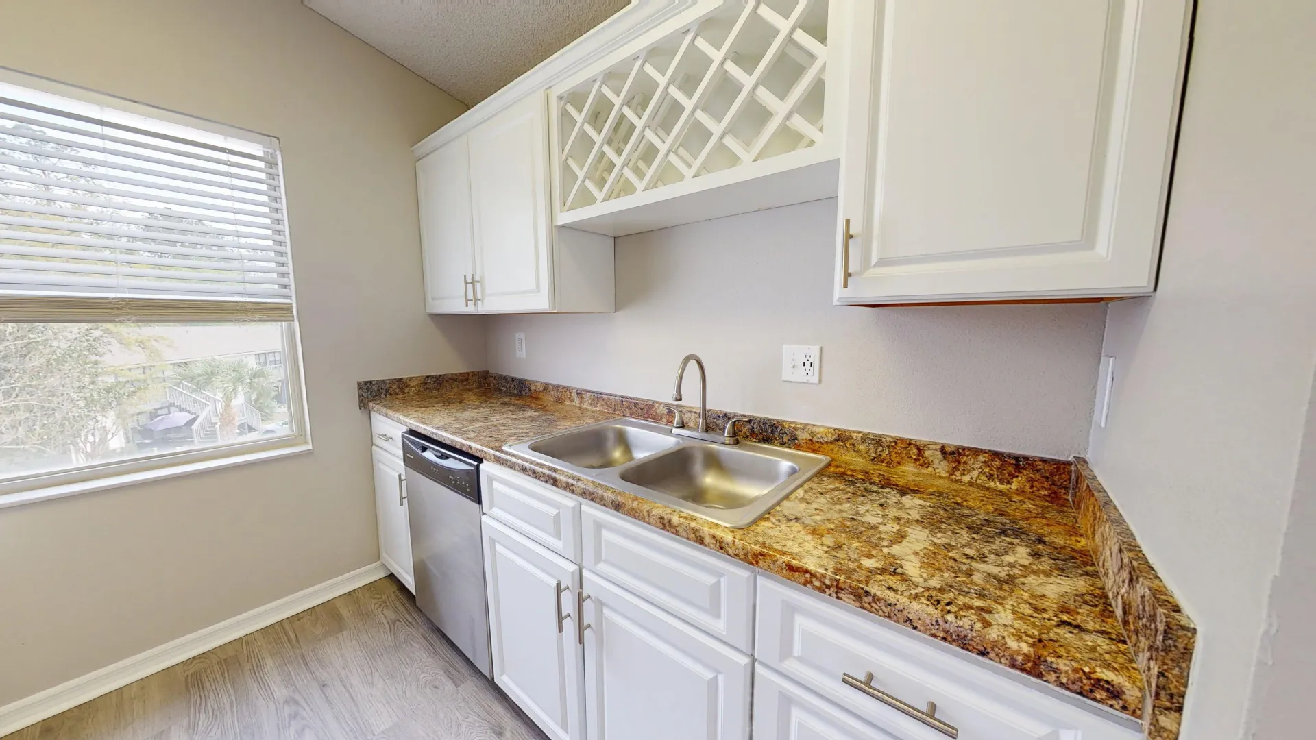 Kitchen in The City floor plan at Ridgemar Commons featuring white shaker-style cabinets, granite-inspired countertops, a double-basin sink, stainless steel dishwasher, and wood-style flooring.