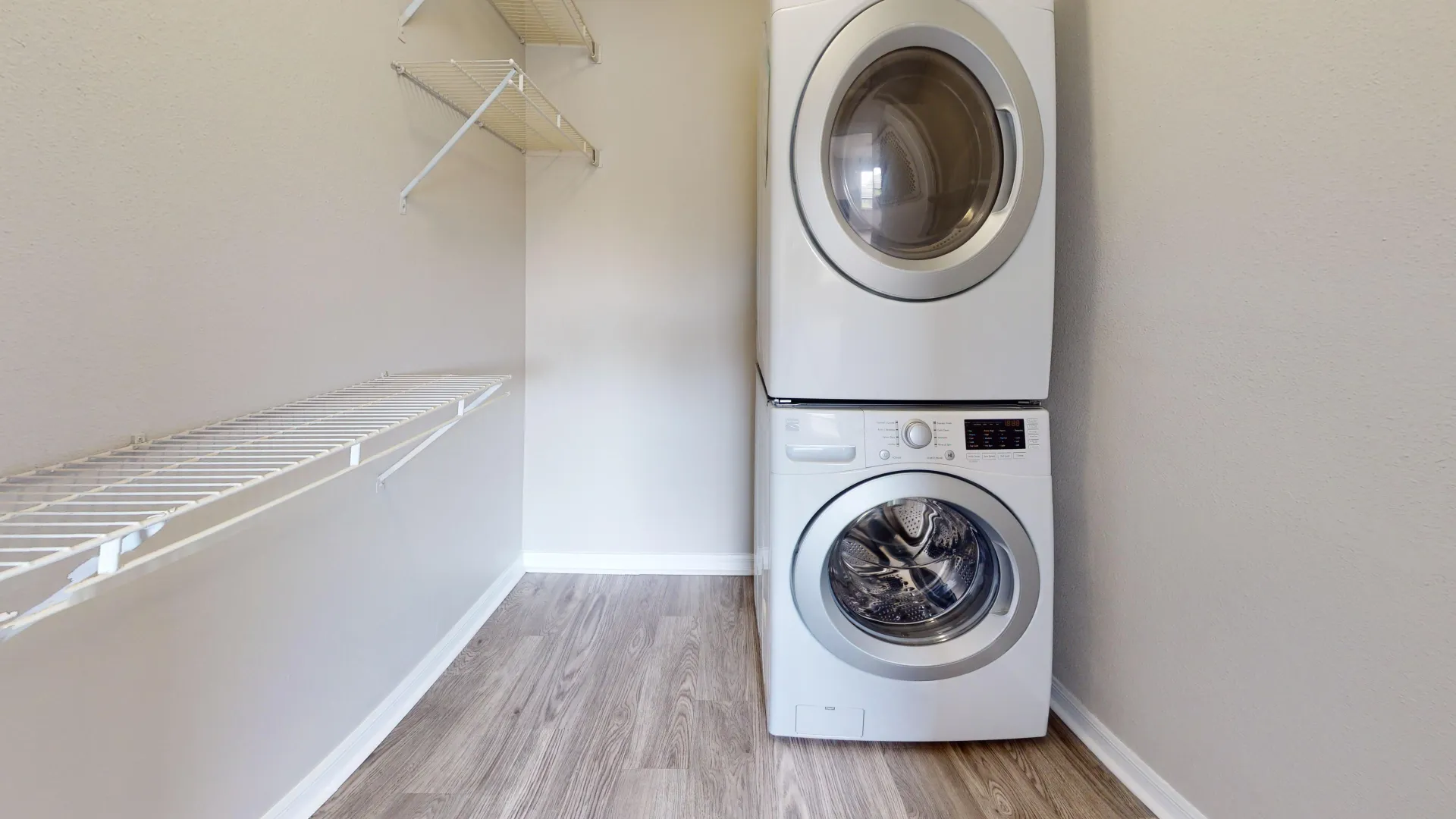 Stackable washer and dryer in The City floor plan at Ridgemar Commons featuring in-home laundry appliances, built-in storage shelving, and wood-style flooring.