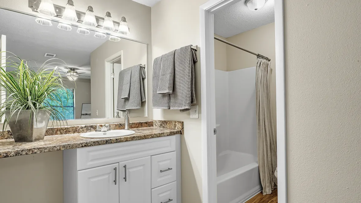 A lavish bathroom adjacent to the master bedroom, presenting a sprawling granite vanity and an expansive mirror, complete with a separate space for the toilet and shower, exuding royal opulence.