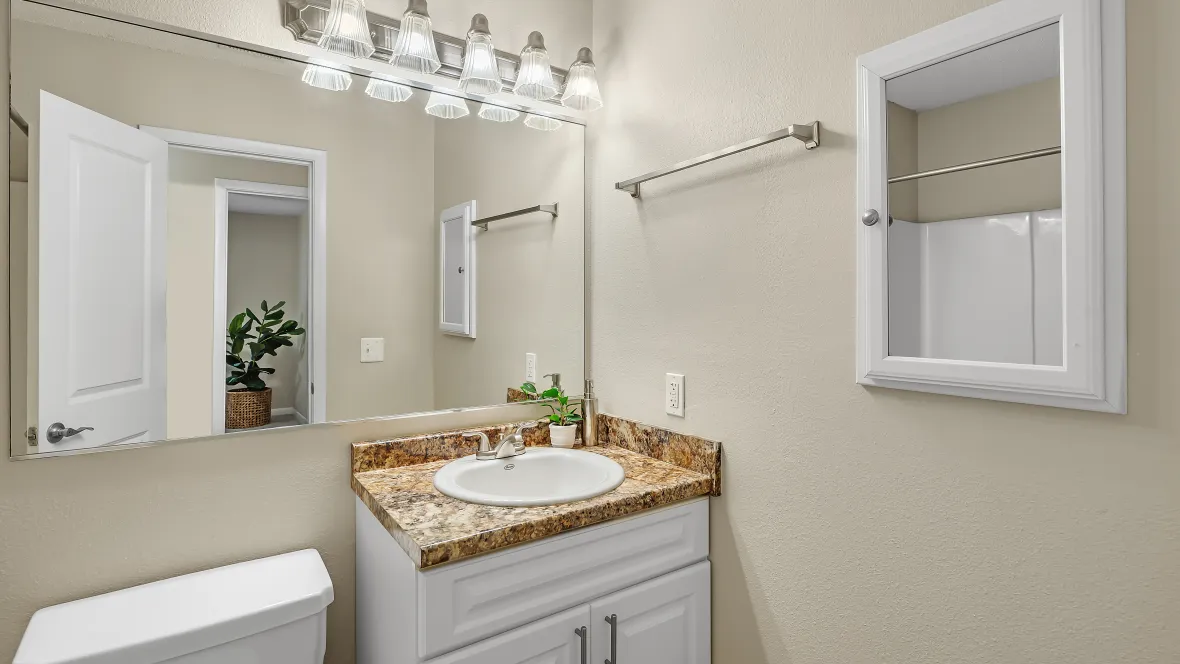 Tranquil bathroom space boasting an elegant granite-inspired countertop, wall-to-wall mirror, and ample overhead vanity lighting with a spacious medicine cabinet with a mirrored door for added brilliance. 