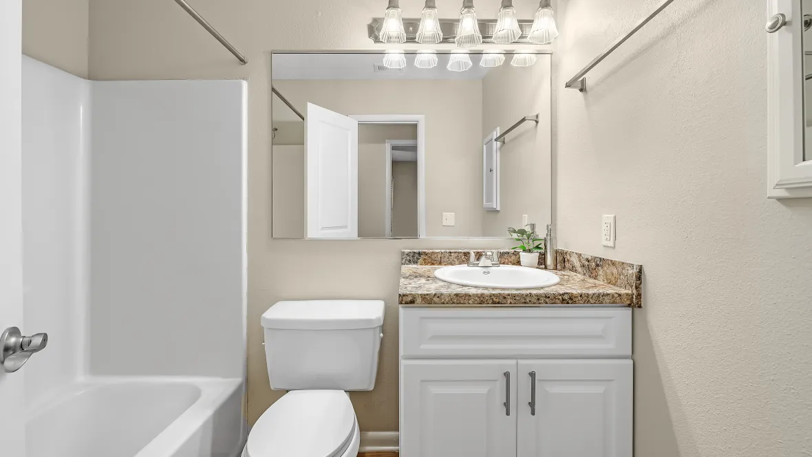 A chic bathroom space showcasing a shower/tub combo next to the toilet with a substantial mirror, granite-style countertops, and a well-appointed mirrored medicine cabinet.