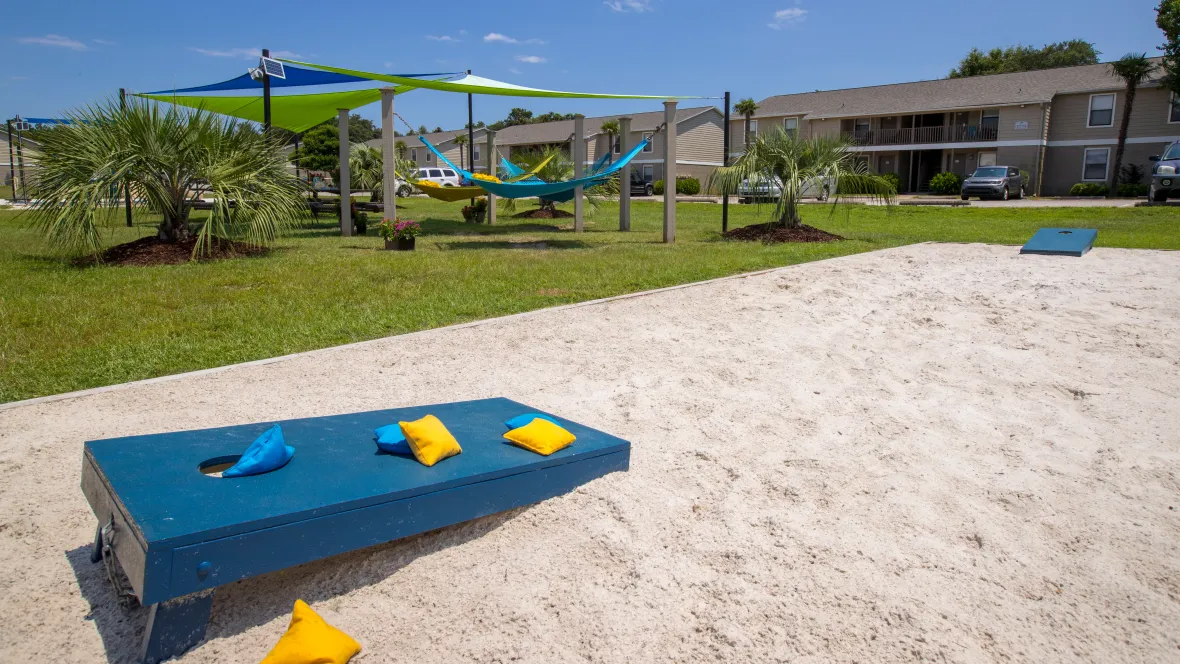 A sand-filled designated cornhole game area adjacent to the hammock garden, offering a space for leisure and outdoor games.