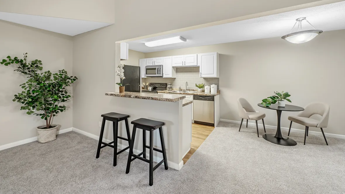 A chic breakfast bar extending from sleek granite-like countertops, adorned with two stylish stools, offering a well-lit connection between the kitchen and dining room.