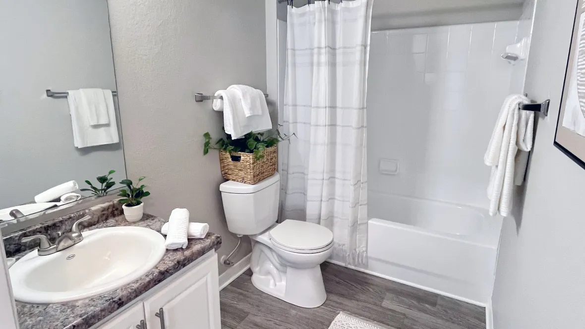 Elegant bathrooms featuring wood-style flooring, granite-style countertops, large mirrors, and a white-tiled shower/tub surround.