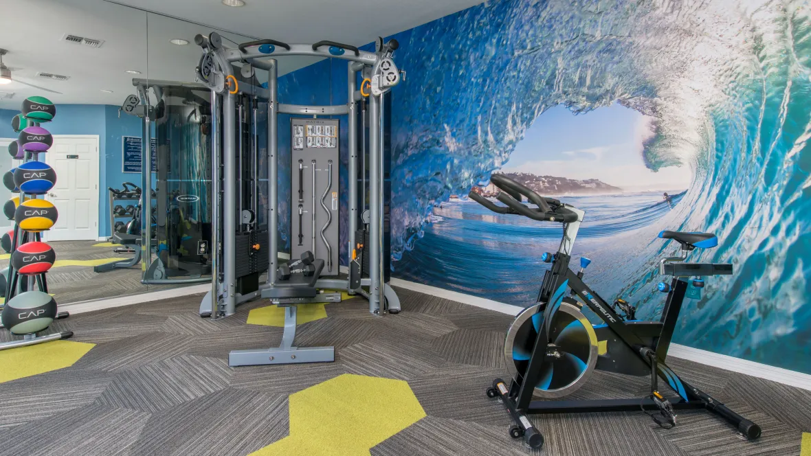 A resident gym with an ocean wave mural wall inspiring adventure and a variety of workout machines including a weight-training machines and spinning bike.