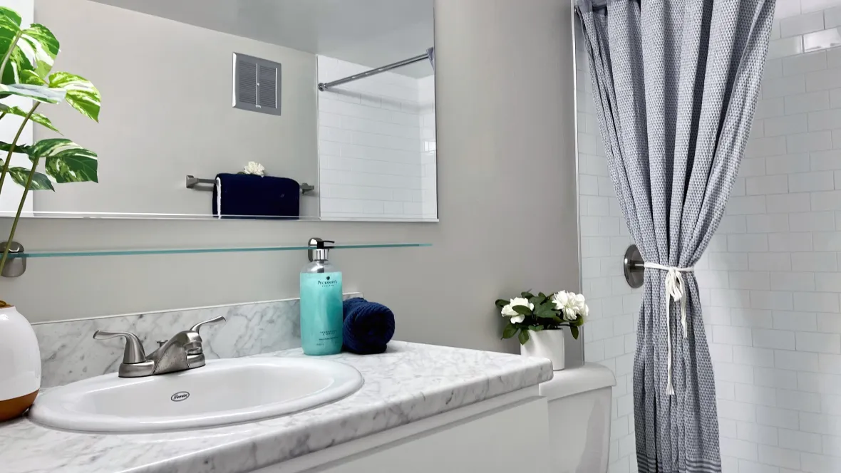 An inviting, chic bathroom updated with refined finishes including gleaming marble-inspired countertops, large mirrors, and a tiled surround shower.