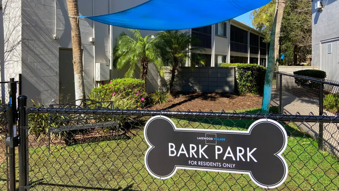 A fenced-in dog park with a sail shade and benches, providing shaded comfort for pet parents while their pups romp and play.
