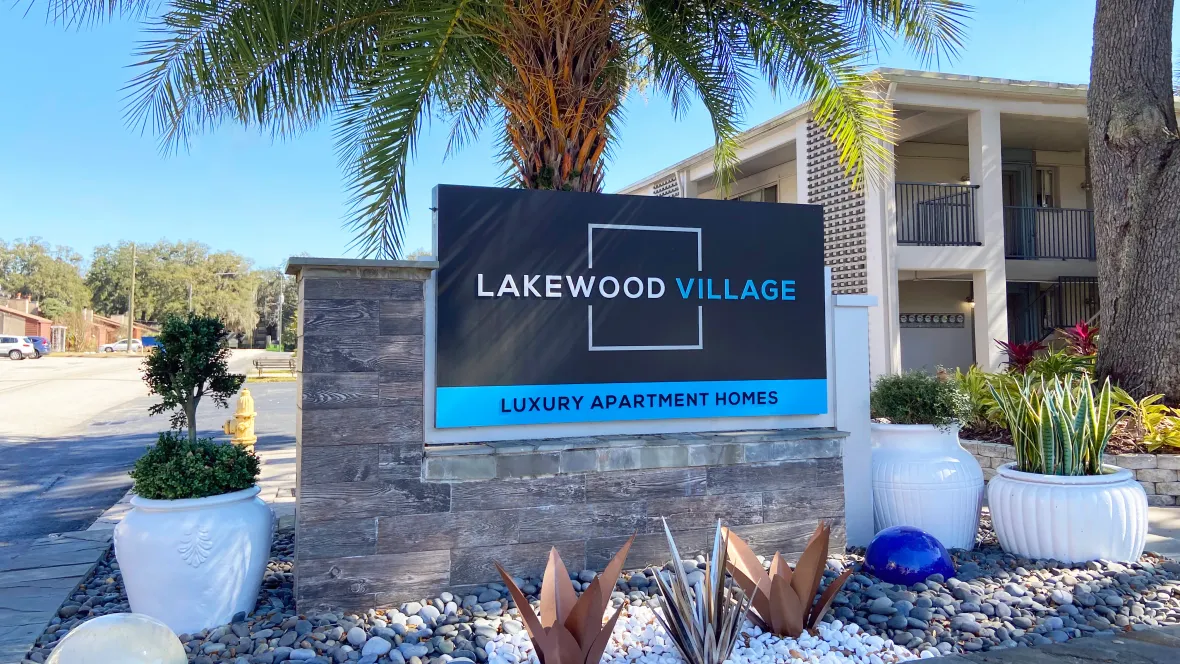 A prominent monument sign at the front entrance adorned with landscaped river rocks and large white planters creating a bold and inviting greeting to the community.