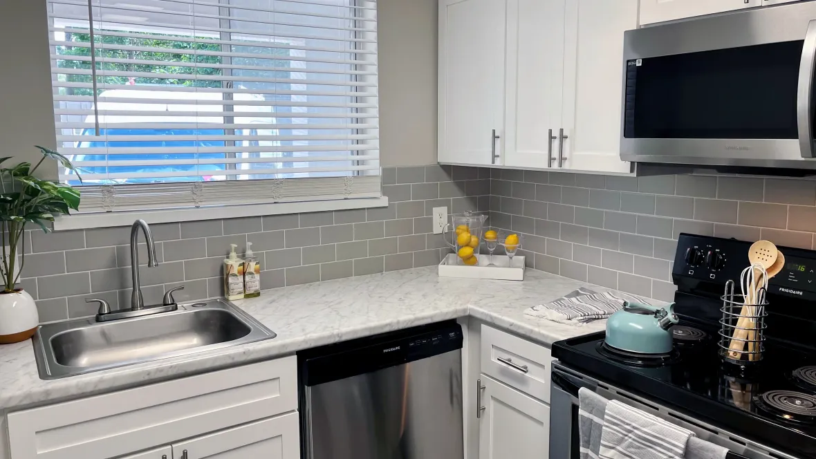 A kitchen with a grey-and-white color scheme including white countertops marbled with grey streaks and a bold grey tile backsplash, showcasing a trendy and stylish design.